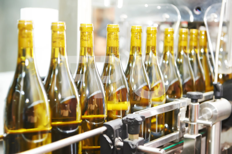 Row of wine bottles with yellow caps on an automated production line in a bottling factory.