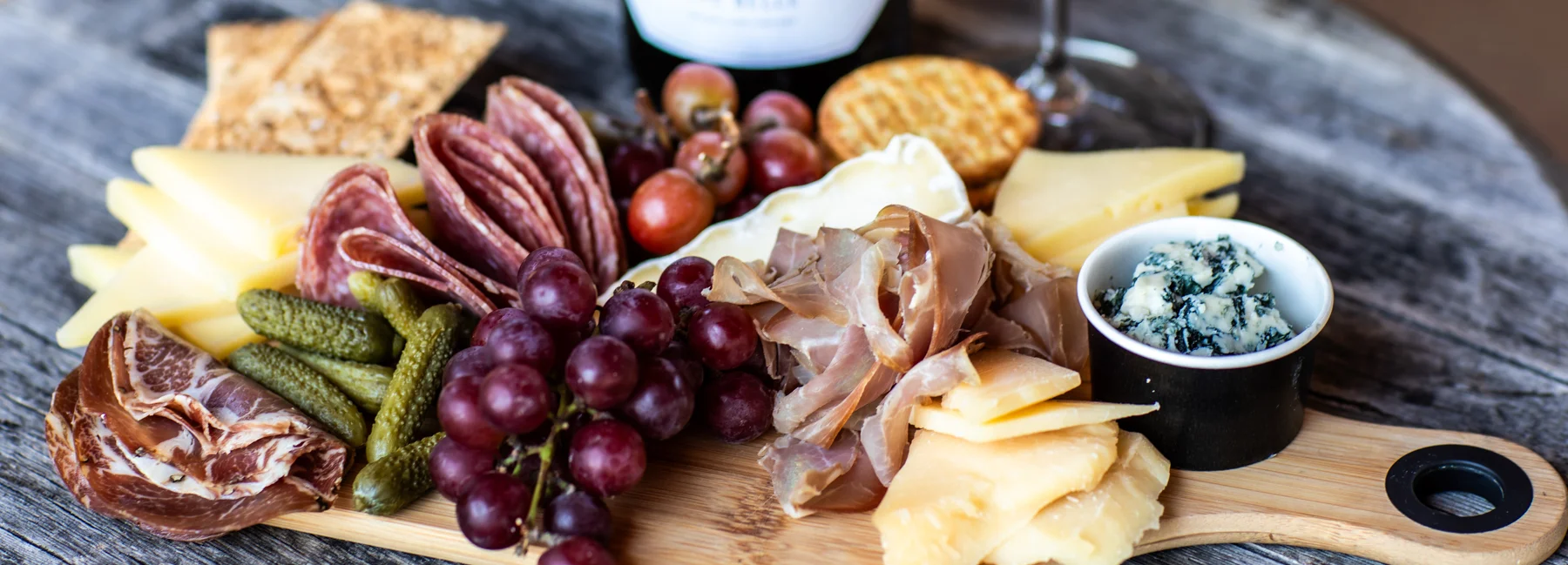 A charcuterie board with cheeses, cured meats, grapes, pickles, crackers, and a small bowl of blue cheese.