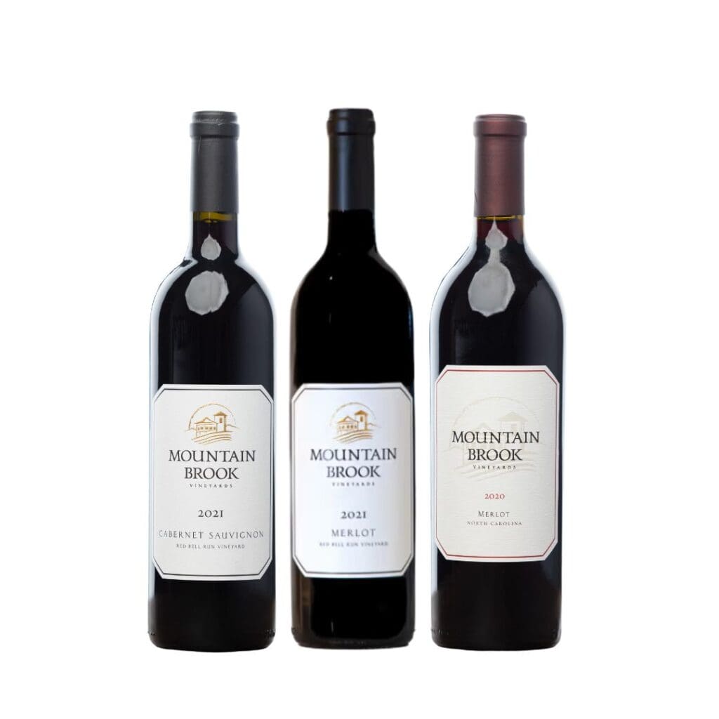 Three bottles of Mountain Brook wine: two Merlots and one Cabernet Sauvignon, all with white labels.