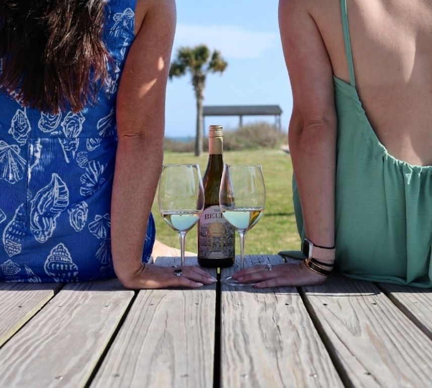two women in dresses with glasses of white wine in their hand looking at the ocean in emerald isle north carolina